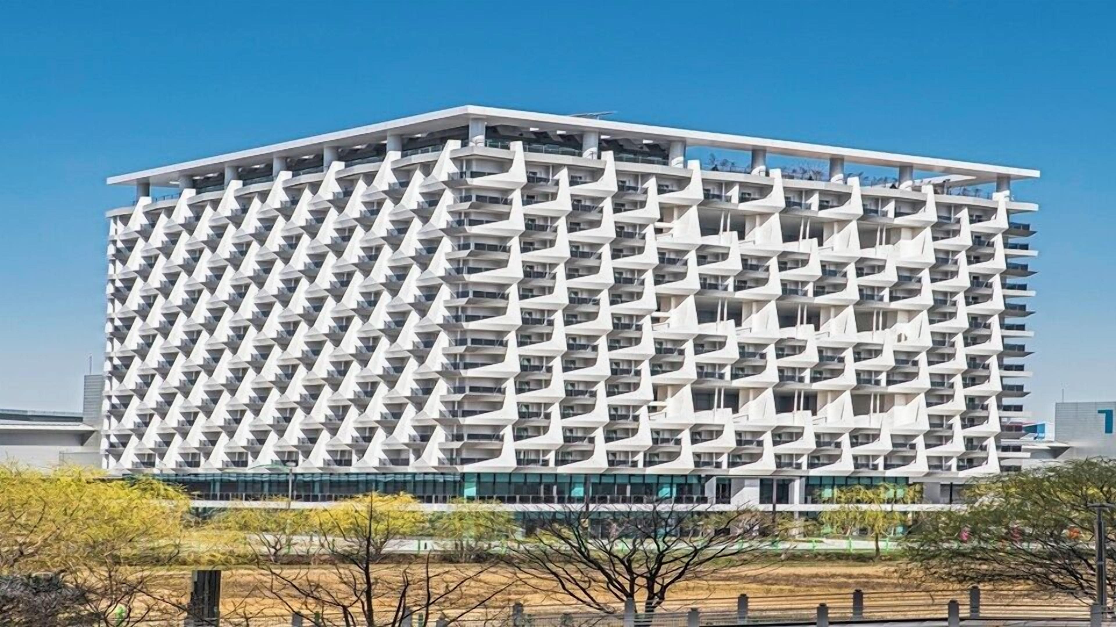 A modern high-rise building with a unique geometric facade, multiple balconies, and a flat roof.