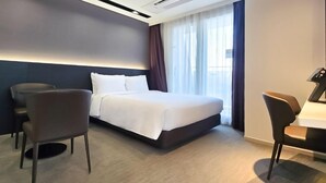Une chambre d’hôtel moderne avec un grand lit, deux fauteuils, un bureau et une fenêtre avec des rideaux.