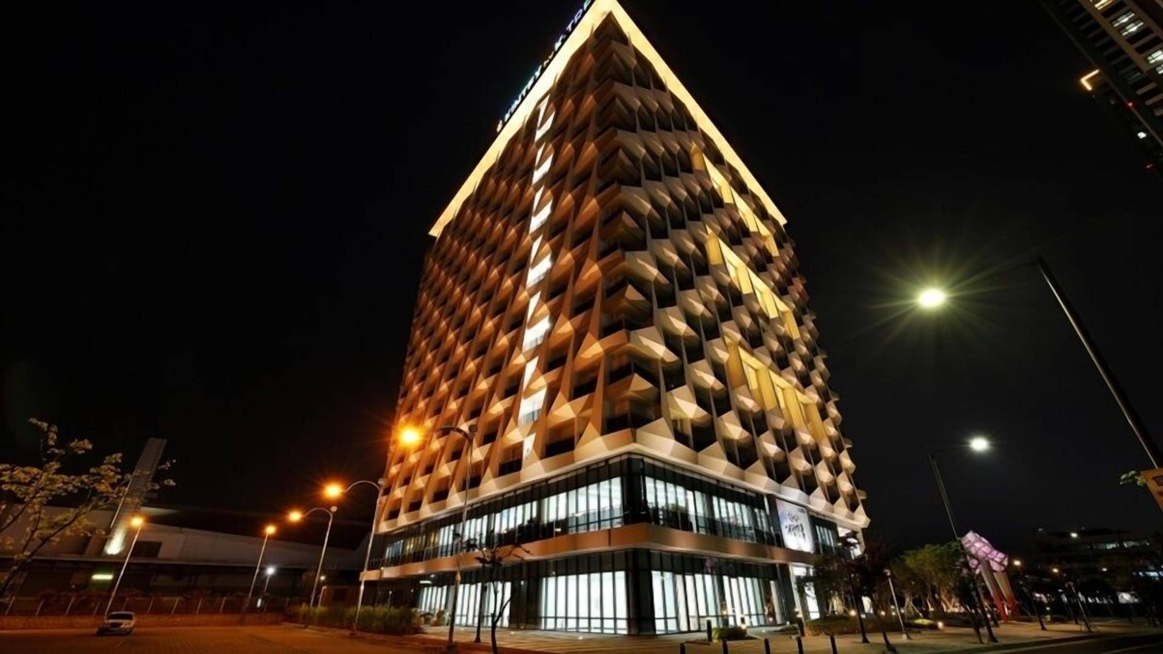 A modern high-rise building with a unique geometric facade and illuminated windows at night.