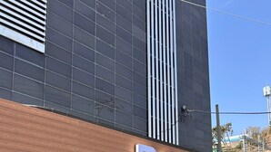 L’entrée d’un hôtel, avec une façade moderne, une grande enseigne indiquant « BAY HOTEL » et une porte de garage ornée d’inscriptions en coréen.