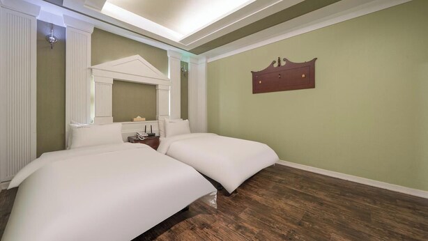 Une chambre avec un lit double, un plancher en bois, un luminaire au plafond et une étagère fixée au mur.