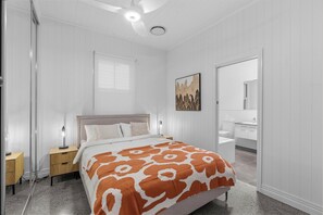 A bedroom with a bed, bedside tables, a nightstand, a window, a painting, and a bathroom with a sink and mirror. - Elegant Dual-Level Home Near Cafés, Parks & River (East Brisbane)