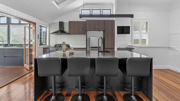 A modern kitchen with a central island, bar stools, and a view of the outdoor area. - Elegant Dual-Level Home Near Cafés, Parks & River (East Brisbane)