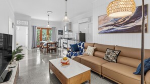 A modern living room with a sofa, coffee table, and a dining area in the background. - Elegant Dual-Level Home Near Cafés, Parks & River (East Brisbane)