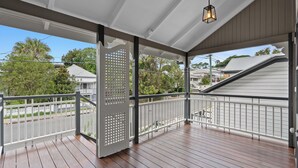 A wooden deck with a white railing, a hanging light fixture, and a view of neighboring houses and trees. - Elegant Dual-Level Home Near Cafés, Parks & River (East Brisbane)