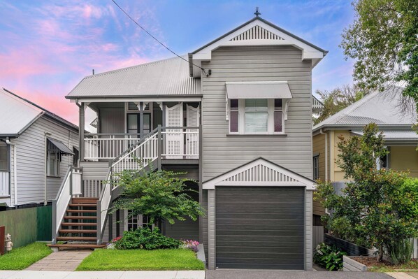 A two-story house with a front porch, a garage, and a staircase leading to the upper floor. - Elegant Dual-Level Home Near Cafés, Parks & River (East Brisbane)
