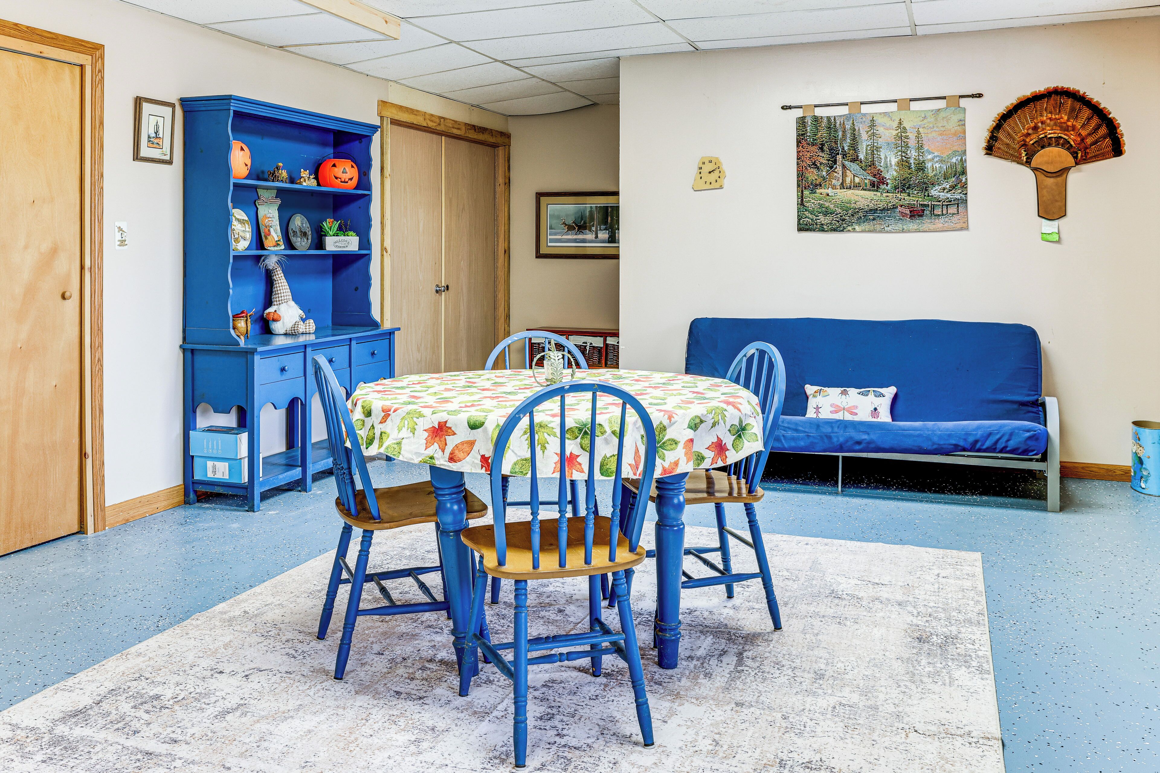 Un comedor con una mesa lista para cuatro personas, rodeada por sillas azules, un sofá azul y un aparador azul con objetos decorativos.