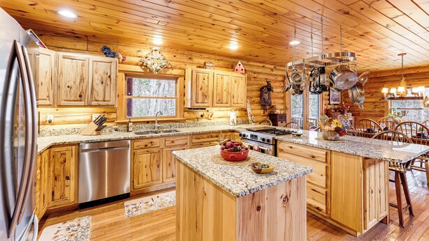 A spacious kitchen with wooden cabinets, stainless steel appliances, and a granite countertop. - Spacious Log Home w/ 13 Acres, Ponds & Fire Pit! (Kingsley)