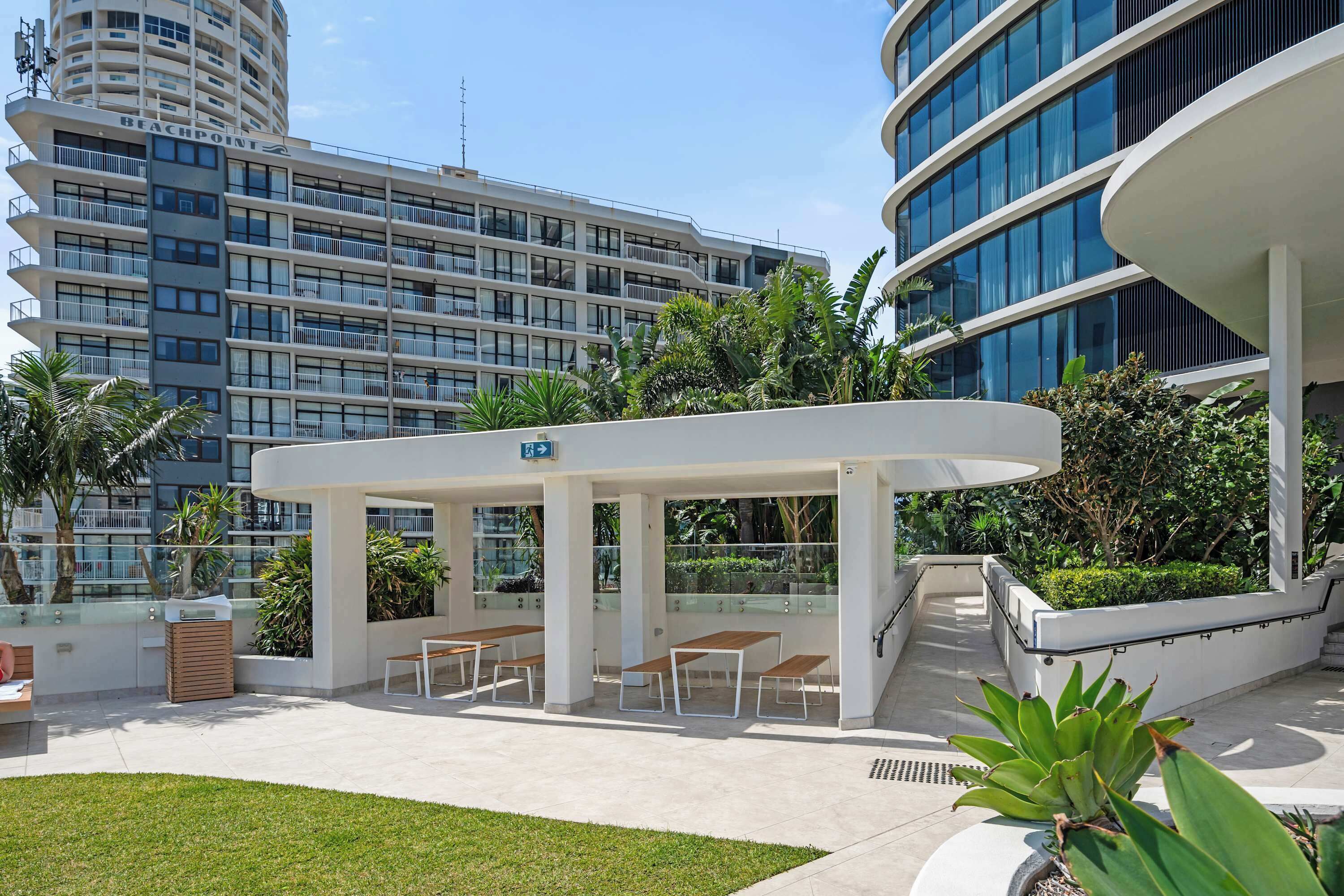 A rooftop terrace with outdoor seating, surrounded by lush greenery and modern buildings.