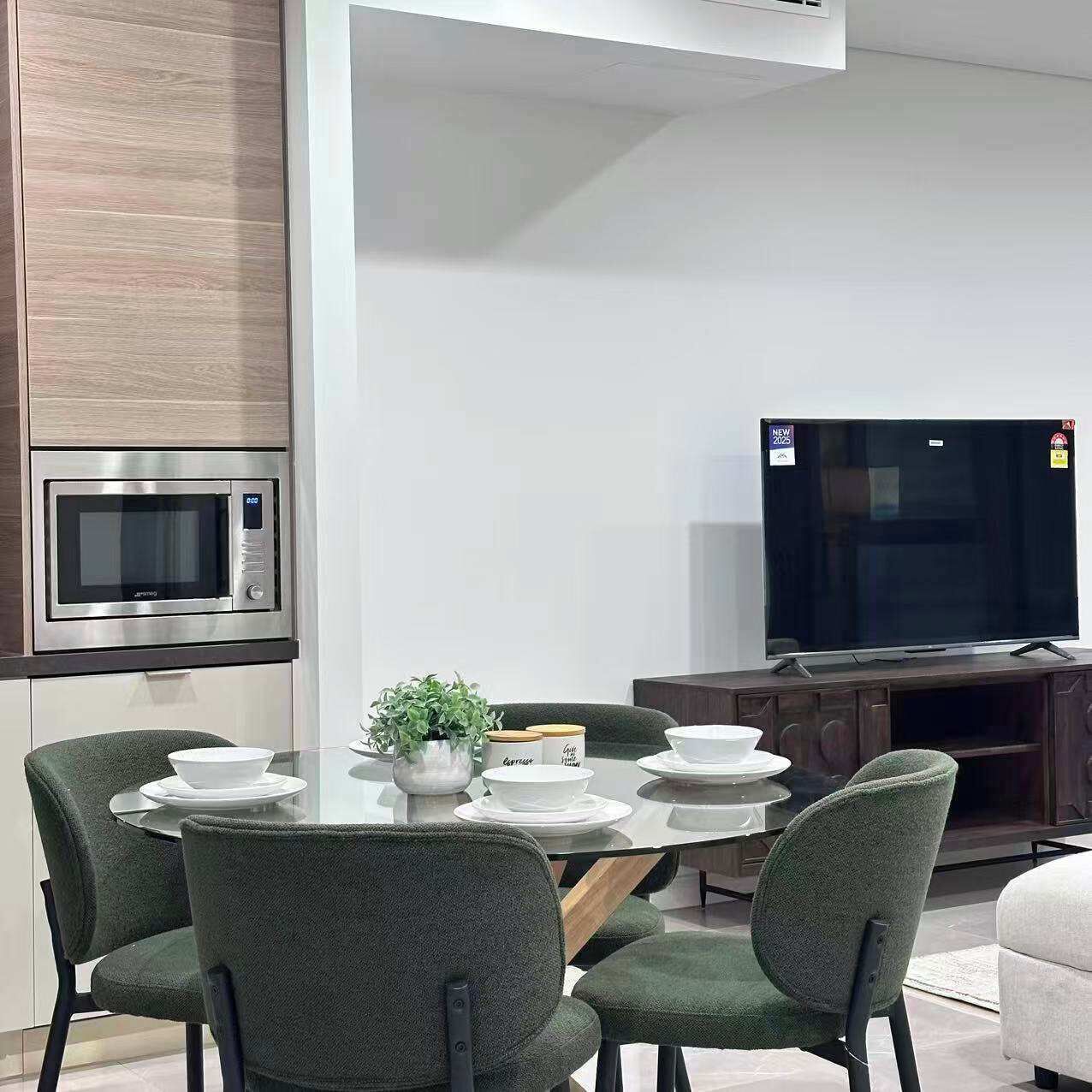 A modern kitchen with a microwave, a dining table with chairs, a television, and a coffee machine.