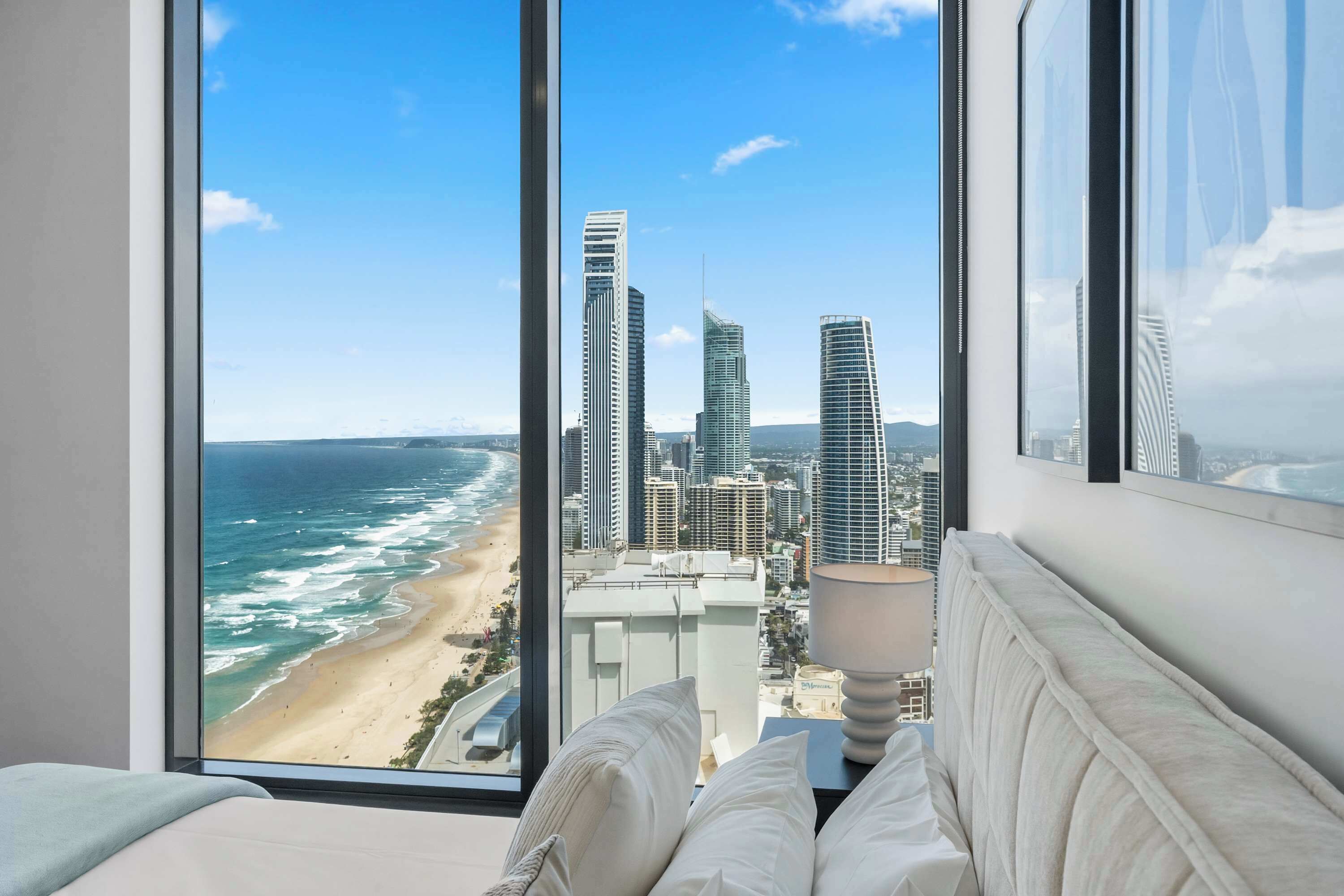Habitación de hotel con un amplio ventanal con vistas a la playa y al horizonte urbano.