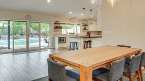 A modern kitchen with a wooden dining table and bar stools, a large island, and a view of a swimming pool. - Close to Hiking! Snowbird Haven w/ Pool in Phoenix (Phoenix)
