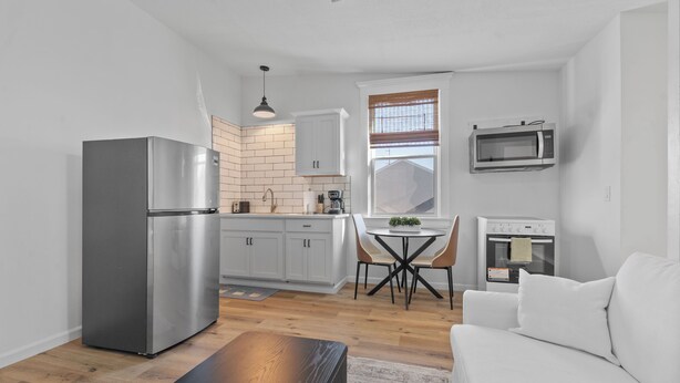A compact kitchen with a refrigerator, microwave, oven, and a dining area with a table and chairs. - Luxe Living Suites #3, 3 minutes to DT Cincy (Covington)