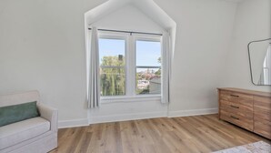 A room with a sloped ceiling, a large window with curtains, a wooden dresser, and a light-colored sofa. - Luxe Living Suites #3, 3 minutes to DT Cincy (Covington)