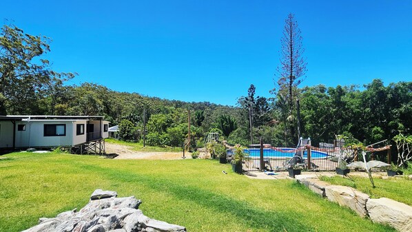 A mobile home with a fenced backyard, a small pool, and surrounding greenery.