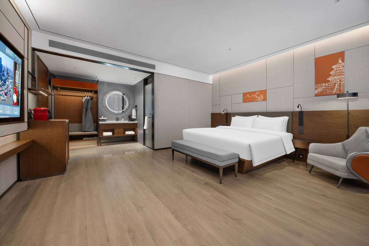 Une chambre d’hôtel moderne dotée d’un grand lit, d’un coin salon, d’une télévision et d’une salle de bain avec un miroir et un porte-serviettes.