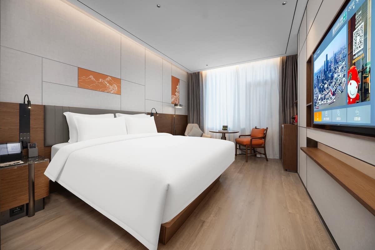 Une chambre d’hôtel moderne dotée d’un grand lit, d’un bureau avec un ordinateur, d’une télévision et d’une petite table avec des chaises.