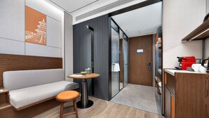 A modern hotel room with a sofa, a small round table with a stool, a wooden cabinet, and a sliding door leading to a bathroom. - UrCove by Hyatt Beijing Zhongguancun Peking University (Beijing)