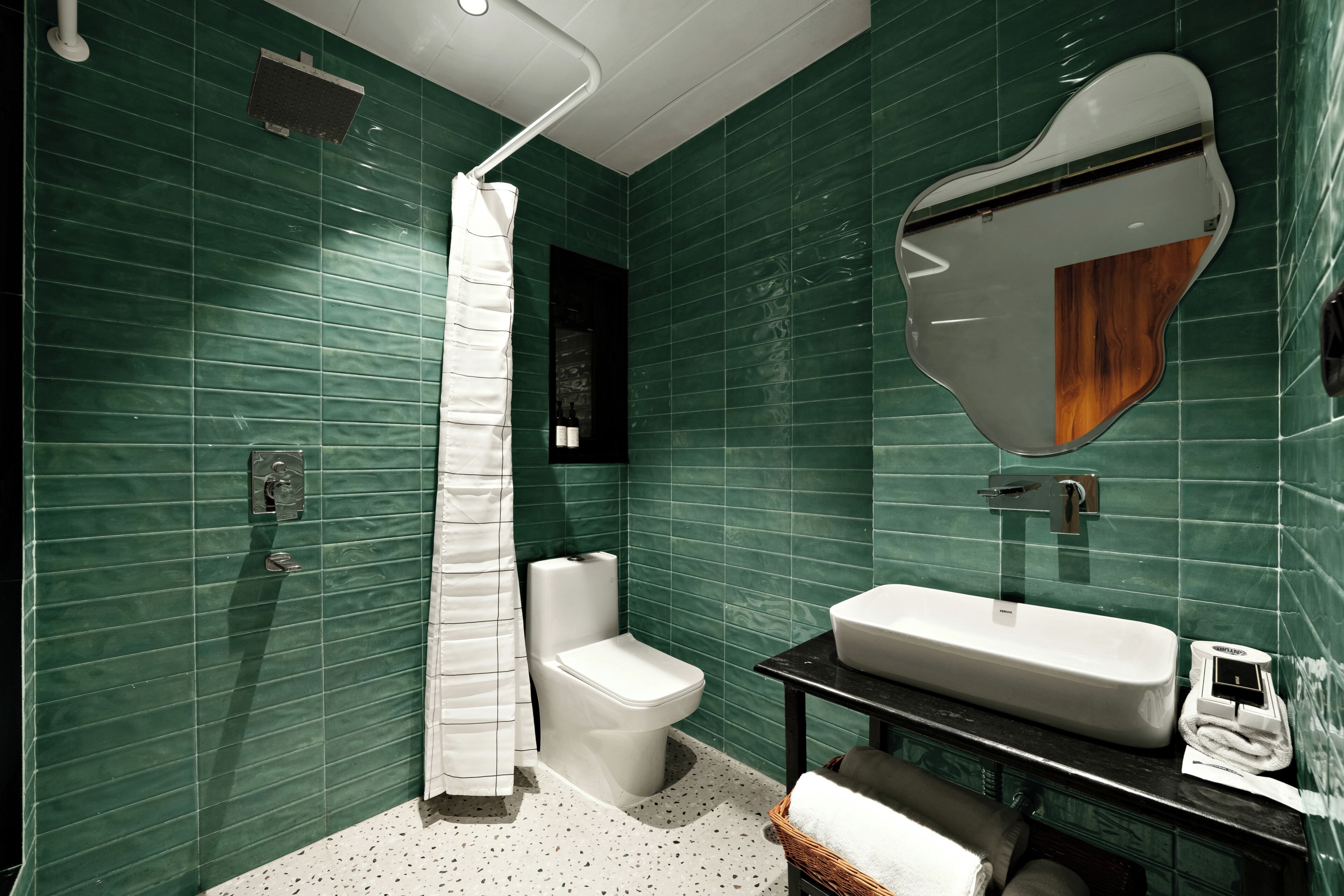 A modern bathroom with green tiles, a white toilet, a shower curtain, a sink, and a mirror.