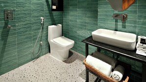 A modern bathroom with green tiled walls, a white toilet, a sink with a mirror, and a towel rack. - The Village Edit - Minimalist Hotels (New Delhi)