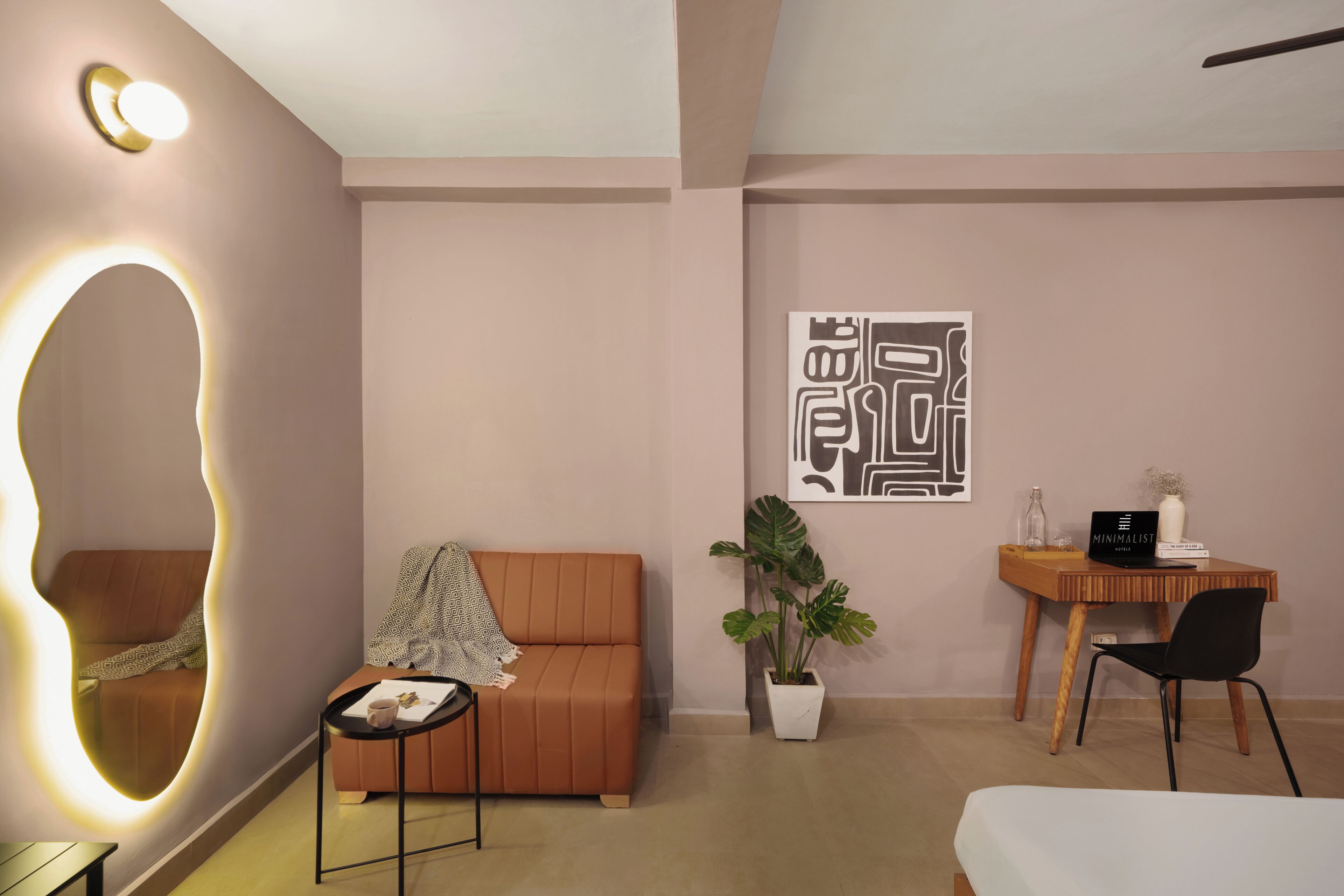 Una habitación moderna con sofá, una mesita, un escritorio con silla, una planta en maceta y un espejo fijado a la pared.