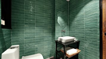 A bathroom with green tiled walls, a white toilet, a black sink on a black shelf, and a wooden door.