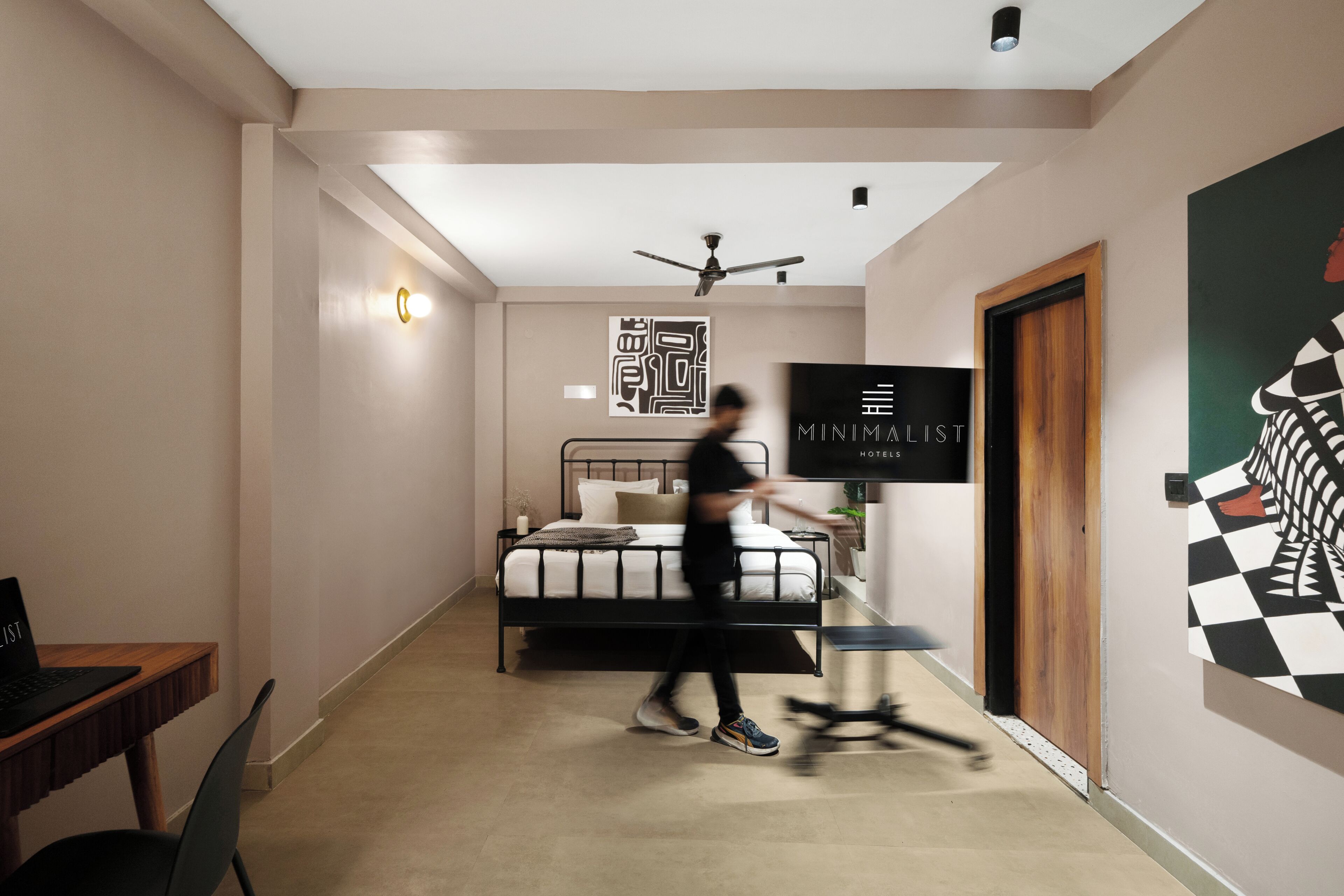Une chambre d’hôtel équipée d’un lit, d’un bureau, d’une chaise, d’un ventilateur de plafond et d’un téléviseur fixé au mur.