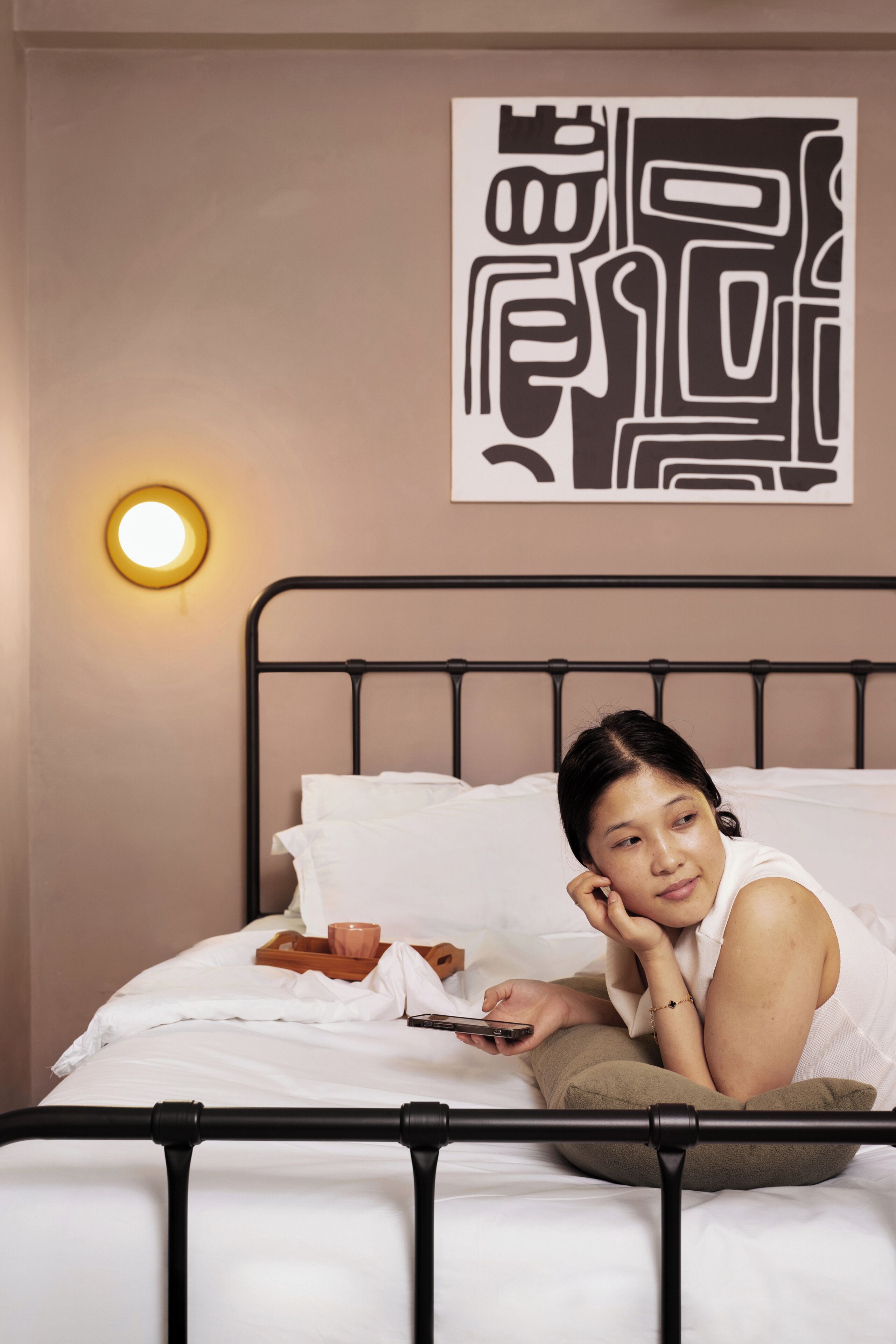 A bed with a metal frame, white bedding, and a wall-mounted light.