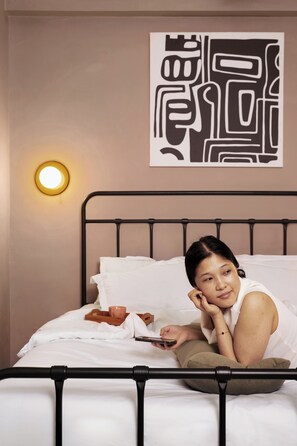 Una cama con estructura metálica, ropa de cama blanca y una lámpara fijada a la pared.