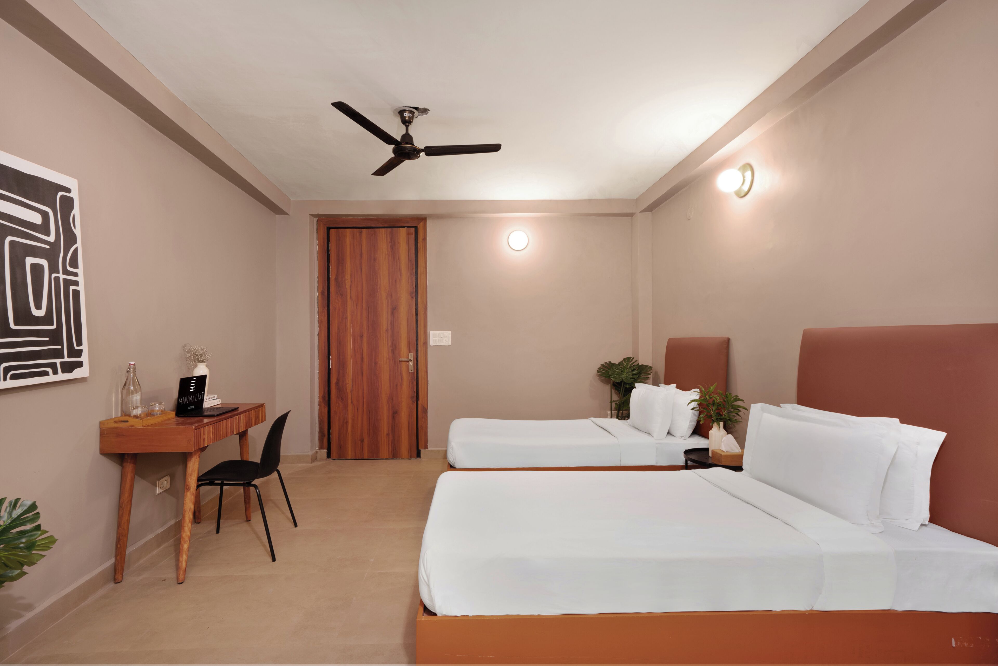 A hotel room with two beds, a desk, a chair, a ceiling fan, and a door.