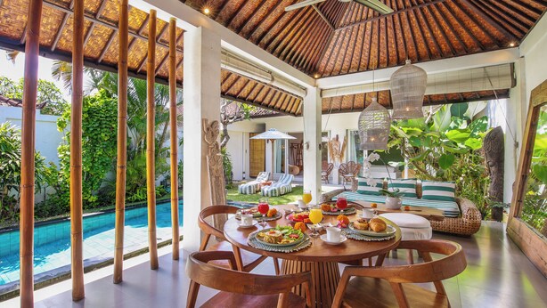 Un espace repas avec vue sur la piscine, des colonnes en bambou et un toit de chaume.