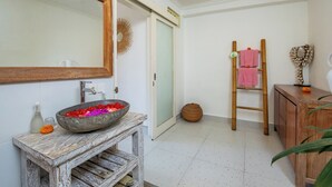 Une salle de bain avec un meuble-lavabo en bois rustique, un grand miroir, un vase rempli de fleurs colorées et une échelle en bois sur laquelle sont posées des serviettes.