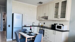 A modern kitchen with a dining table, chairs, a refrigerator, a stove, and cabinets. - Stylish 1 Bedroom Big Bay Apartment walking distance from the beach (Cape Town)