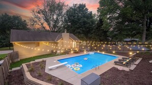 Ein Garten mit Swimmingpool, Liegestühlen und Lichterketten.