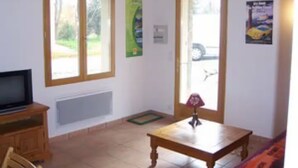 Una stanza con televisore su un mobile in legno, un tavolino con un vaso e due finestre con stipiti in legno.
