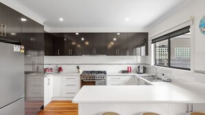 Uma cozinha moderna com armários escuros, geladeira de aço inoxidável, fogão a gás e uma grande janela com vista para a cidade.