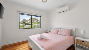 Quarto com cama, janela, mesa de cabeceira, abajur e ar condicionado.