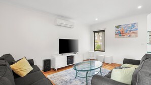 Uma sala de estar moderna com televisão de tela plana, móveis brancos e uma mesa de centro de vidro.