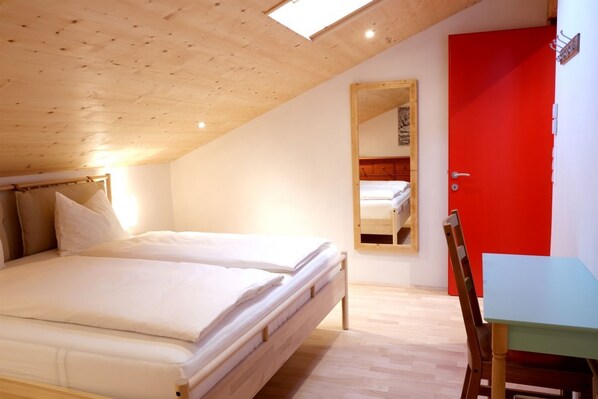 Une chambre avec deux lits, une porte rouge, une petite table et un miroir.
