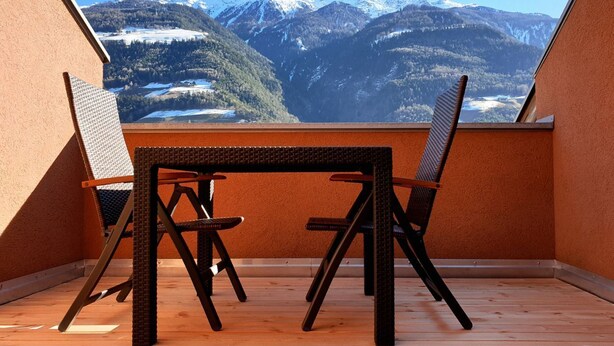 A balcony with a table and chairs, offering a view of snow-capped mountains. - Apartment Luam - Alpstay (Naturno)