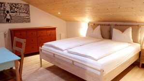A bedroom with a wooden ceiling, a bed with white bedding, a red dresser, and a small table with a chair. - Apartment Luam - Alpstay (Naturno)