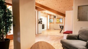 A modern interior with a wooden ceiling, a dining area with a table and chairs, a grey sofa, and a large potted plant. - Apartment Luam - Alpstay (Naturno)