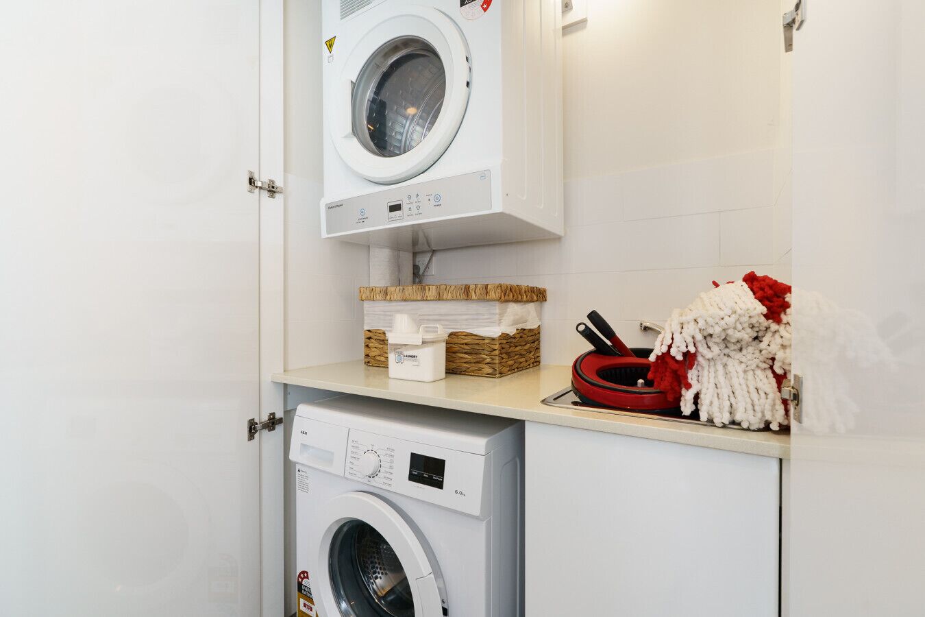 Une buanderie équipée de deux machines à laver, d’un panier contenant de la lessive et d’un porte-serviettes rouge et blanc.