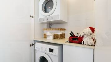 Une buanderie équipée de deux machines à laver, d’un panier contenant de la lessive et d’un porte-serviettes rouge et blanc.