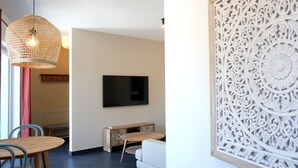Ein modernes Wohnzimmer mit Flachbildfernseher, einer gewebten Pendelleuchte, einem Holzschrank und einer dekorativen Wandverkleidung.