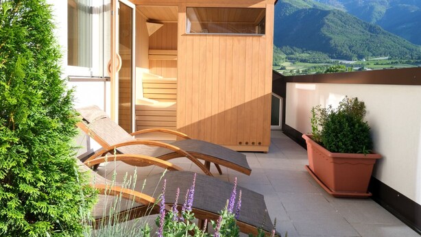 Ein Balkon mit Holzmöbeln, einem Blumentopf und Blick auf Berge.