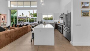 A spacious kitchen with a central island, modern appliances, and large windows offering views of the outdoors. - Miracle Retreat (Palm Springs)