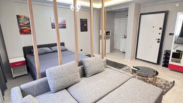 A modern living room with a grey sofa, a bed, and a dining area.