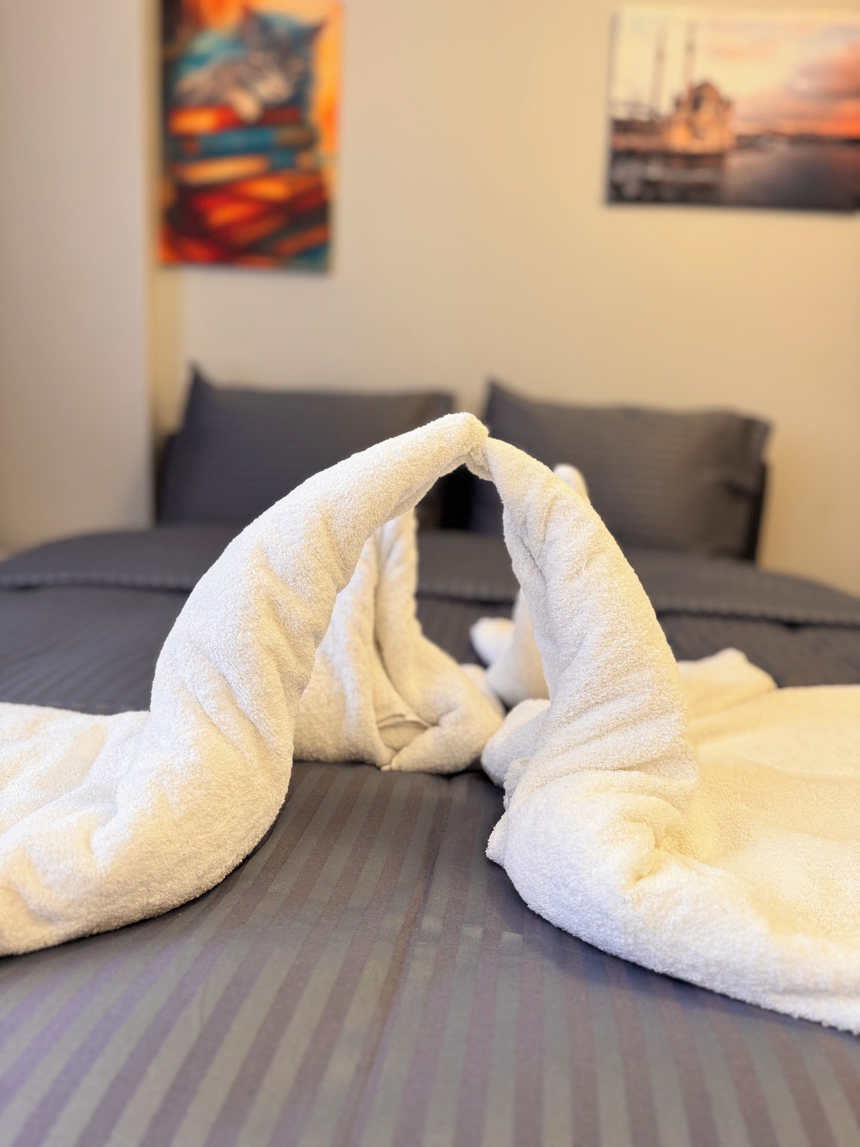 Una cama con una colcha blanca doblada de forma inusual, un colchón gris y un cuadro en la pared.