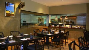A restaurant with a view of the kitchen, wooden tables and chairs, and a fan on the wall. - Seaport Negombo (Negombo)